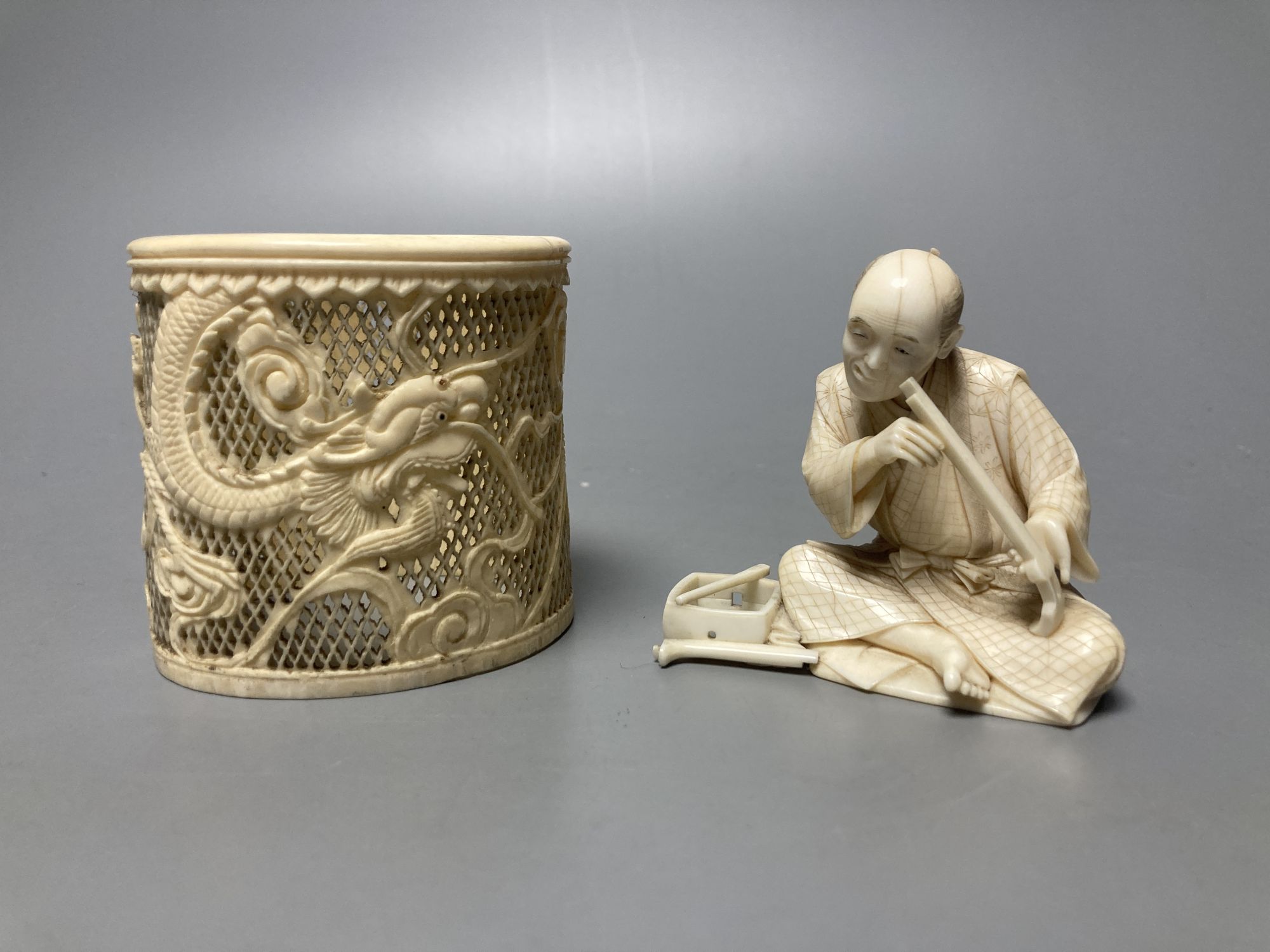 A Japanese ivory okimono of a furniture maker, signed tablet to base, Meiji period and a Chinese pierced ivory sleeve, height 6cm